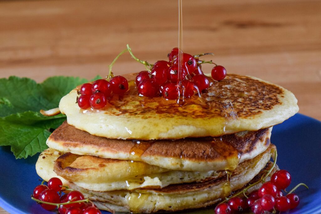 Sugar syrup pouring over pancakes, showcasing utilization of sugar derivatives produced with enzymes in food applications